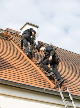 Two chimney sweeps climbing up house roof